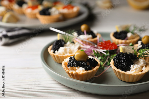 Delicious tartlets with caviar and cream cheese served on white wooden table  closeup