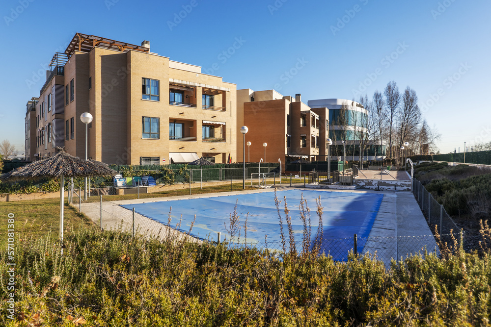 Gardens with a summer pool covered with blue canvas, umbrellas and wooden benches of an urban residential development
