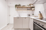 Holiday apartment kitchen with gray base units with stainless steel bowl handles, wooden shelves and small appliances on a white countertop