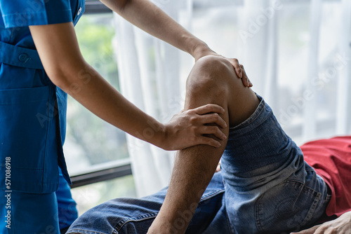 Young man with knee pain doing physiotherapy to rehabilitate leg for immobile patient Serious doctor helping male athlete exercise during rehabilitation after leg injury