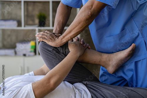 Young man with knee pain doing physiotherapy to rehabilitate leg for immobile patient Serious doctor helping male athlete exercise during rehabilitation after leg injury