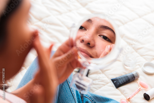 Young girl on her bed, applying face anti-wrinkle cream on her cheek. Skin care at home.