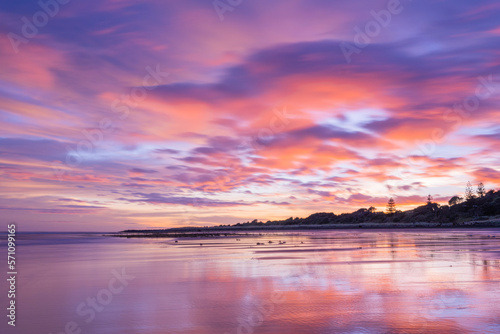 Fitzroy Beach, New Plymouth, New Zealand. Purple clouds at the beach during sunrise with reflections in the water 