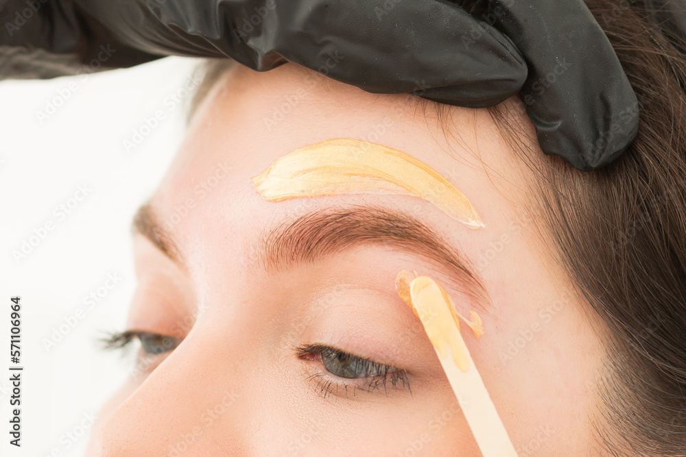 Young woman undergoing eyebrow correction procedure, waxing, wax
