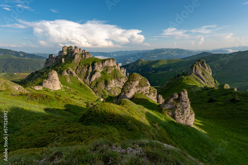 Green meadow with rocks and rocky mountains in romanian mountains in muntii ciucas with setting sun photo