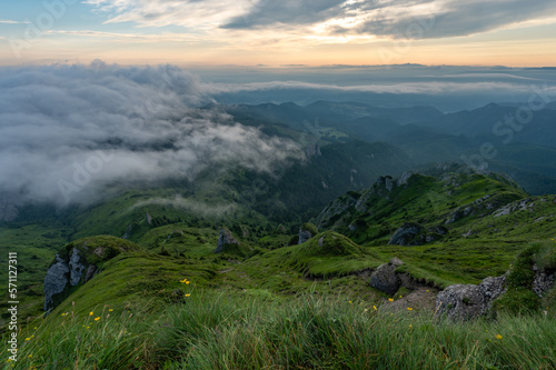 Green meadows with rocks and rocky mountains with fog in the valley and clouds in the sky in romanian mountains in muntii ciucas