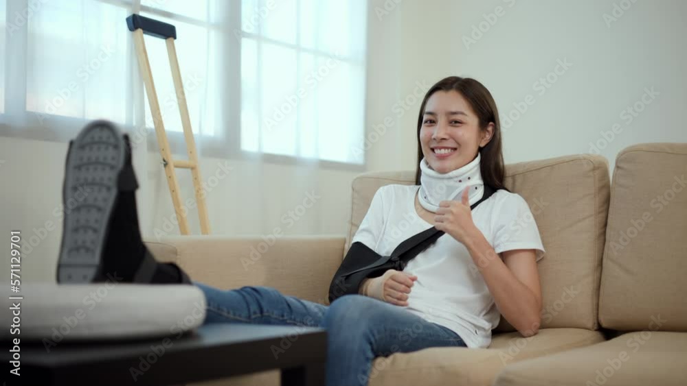 Happy woman recovery from accident fracture broken bone injury with leg splints in cast, neck splints collar, arm splints, sling support arm in living room. Social security and health insurance. Happy woman recovery from accident fracture broken bone injury with leg splints in cast, neck splints collar, arm splints, sling support arm in living room. Social security and health insurance.