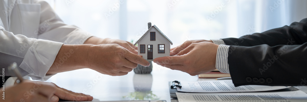 Young Asian real estate agent, and insurance salesman handing over a sample house to a client after signing the sale at the office. - obrazy, fototapety, plakaty 