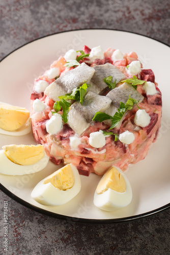 Sillsallad Herring salad with vegetables dressed with sour cream and decorated with boiled eggs close-up in a plate on the table. vertical