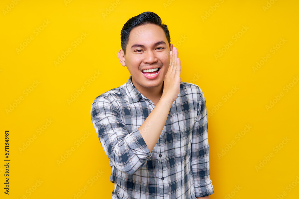 Smiling young handsome Asian man hand on mouth telling secret and whispering gossip isolated on yellow background. People lifestyle concept Smiling young handsome Asian man hand on mouth telling secret and whispering gossip isolated on yellow background. People lifestyle concept