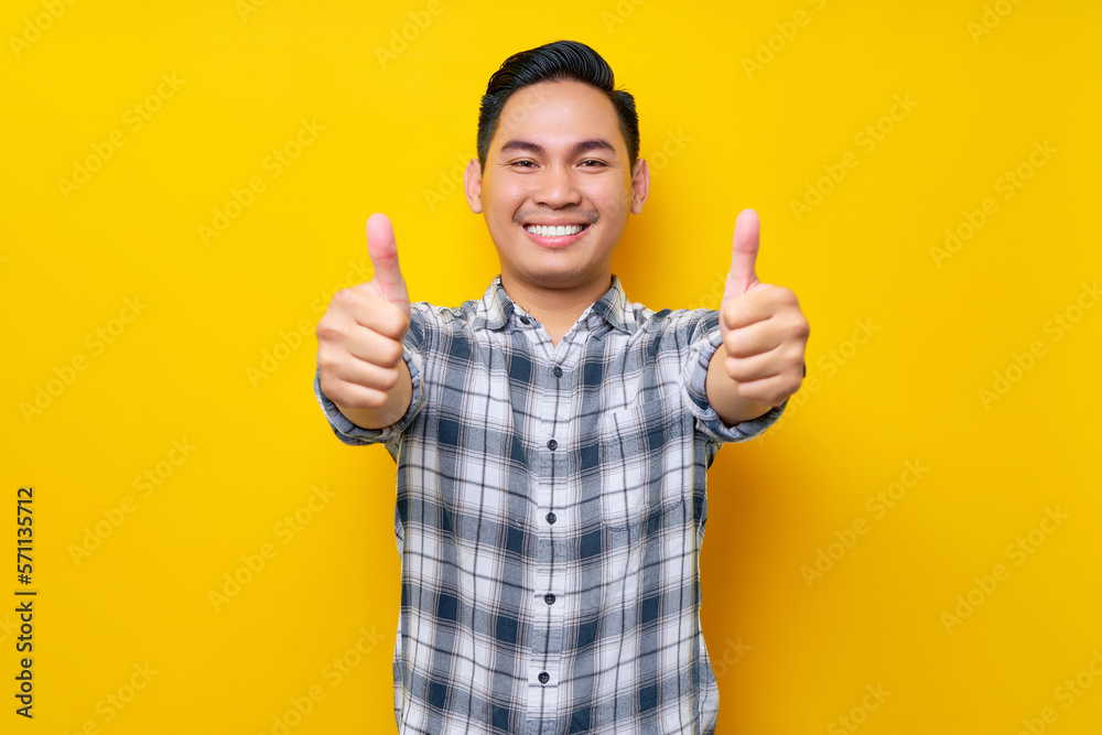 Smiling young handsome Asian man wearing casual clothes showing thumbs up gesture with hand, recommending something good isolated on yellow background. People lifestyle concept Smiling young handsome Asian man wearing casual clothes showing thumbs up gesture with hand, recommending something good isolated on yellow background. People lifestyle concept