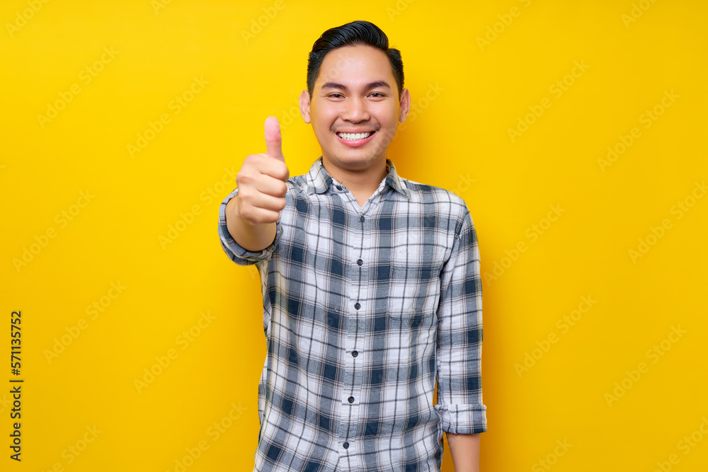 Smiling young handsome Asian man wearing casual clothes showing thumbs up gesture with hand, recommending something good isolated on yellow background. People lifestyle concept Smiling young handsome Asian man wearing casual clothes showing thumbs up gesture with hand, recommending something good isolated on yellow background. People lifestyle concept