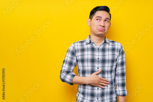 Canvas Print Young handsome Asian man wearing casual clothes keeps his hands on his stomach feeling hungry and wanting to eat delicious isolated on yellow background