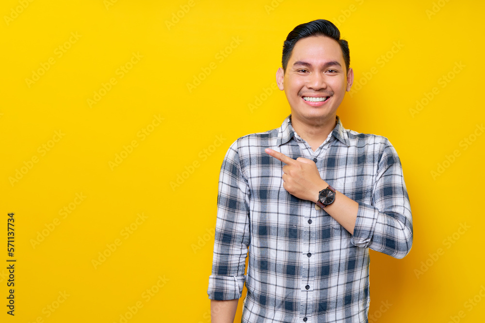 Smiling young handsome Asian man 20s wearing a plaid shirt pointing a finger at the advertising area isolated on yellow background. People lifestyle concept Smiling young handsome Asian man 20s wearing a plaid shirt pointing a finger at the advertising area isolated on yellow background. People lifestyle concept