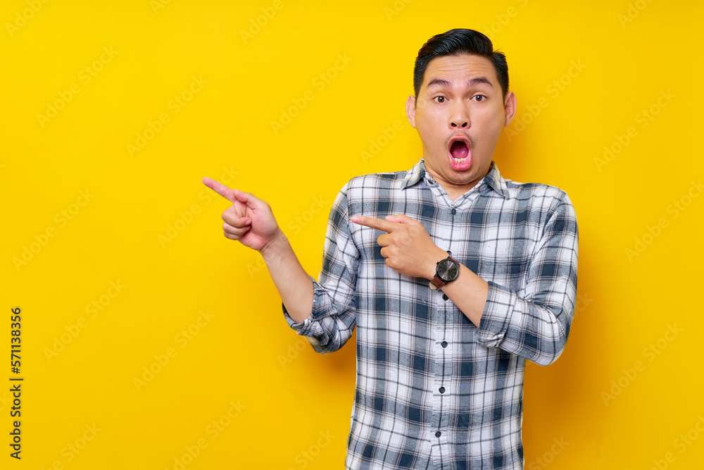 Surprised young handsome Asian man 20s wearing a plaid shirt pointing a finger at the advertising area isolated on yellow background. People lifestyle concept Surprised young handsome Asian man 20s wearing a plaid shirt pointing a finger at the advertising area isolated on yellow background. People lifestyle concept