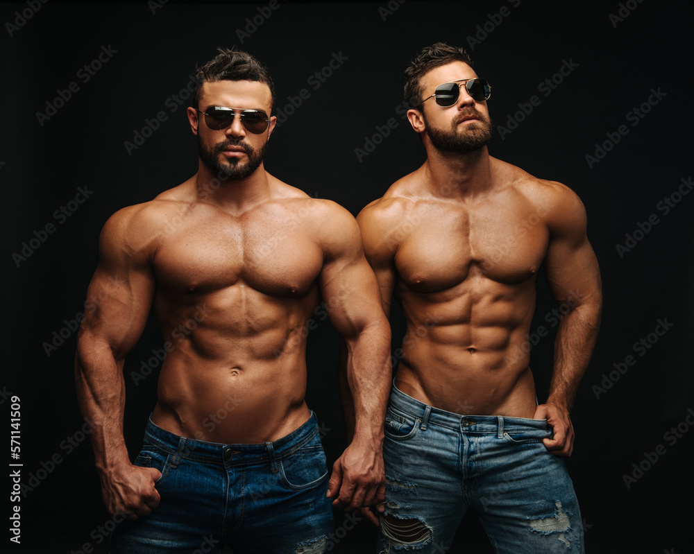 Two shirtless hunks at black background. Fitness models couple in
