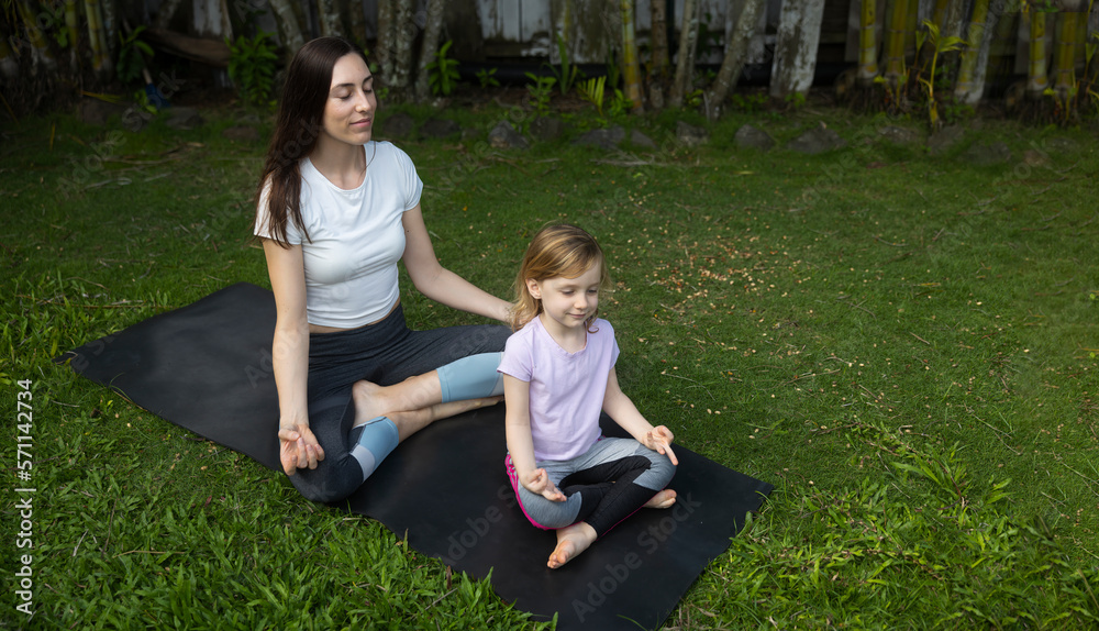 Fototapeta premium Mother and daughter doing yoga pose outside park on a yoga mat