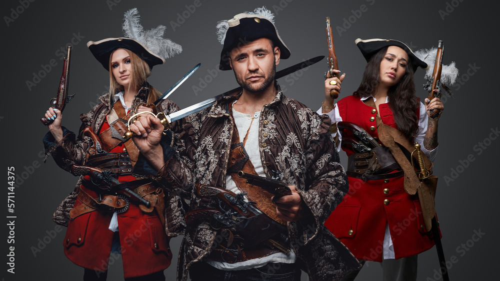 Obraz premium Shot of pirate man and two women with flintlock guns against grey background.