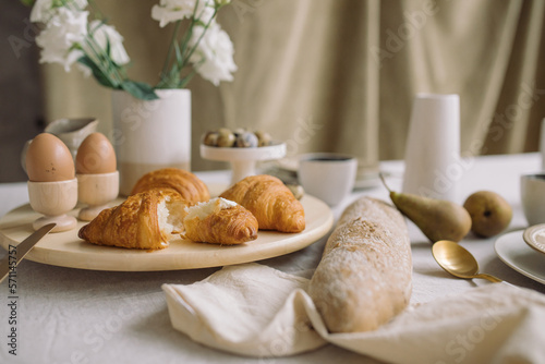 Closeup of delicious breakfast with fresh croissants and french baguette. Elegant crockery and flowers on dining table.