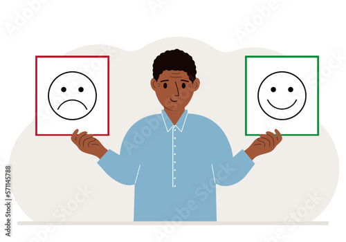 Smiling man holds a card with a sad emoji in one hand and a smiling emoji in the other hand. The concept of emotions, masks or psychological help.