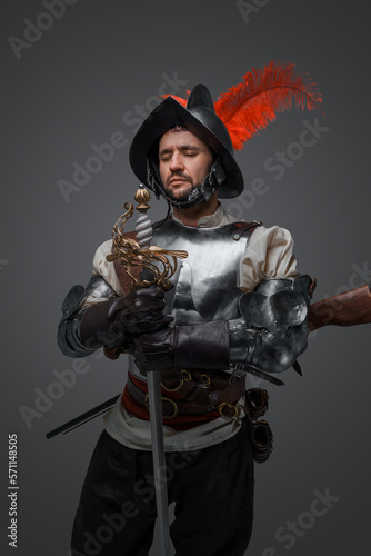 Portrait of medieval musketeer man with plate armor and sword isolated on grey.