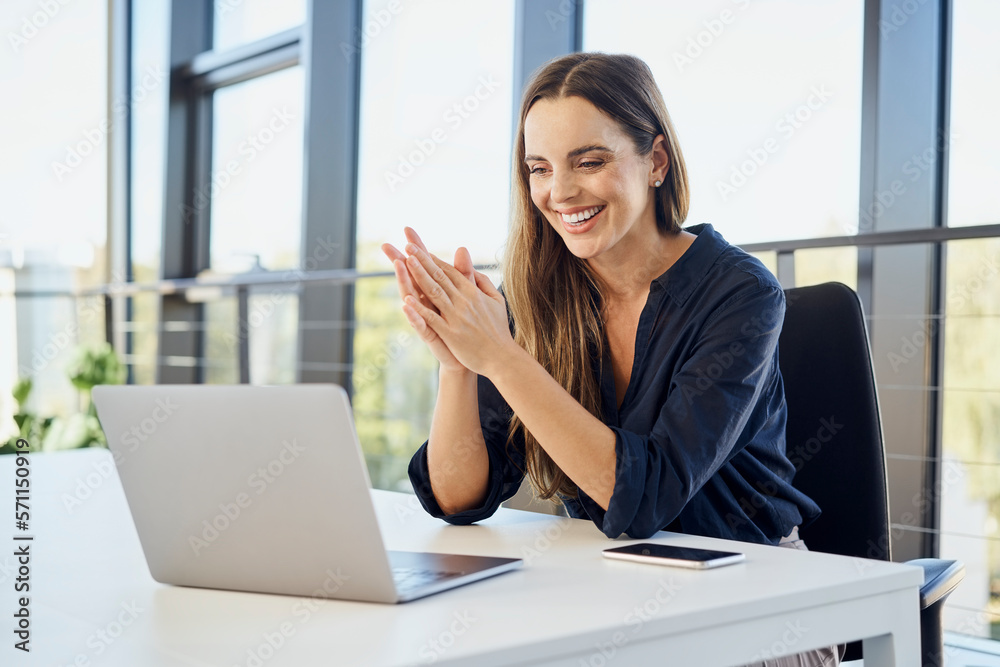 Happy businesswoman with hands clasped doing video call on laptop at office Happy businesswoman with hands clasped doing video call on laptop at office