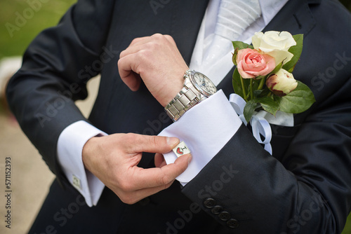the groom adjusts the cufflink on his white shirt
