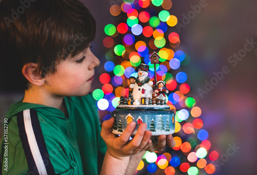 Boy holding Christmas decoration with tree lights in background. photo