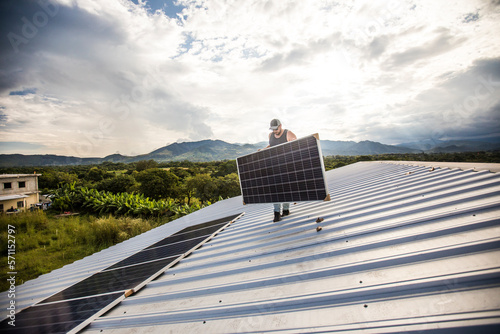 Man carrying solar panel on roof during installation.