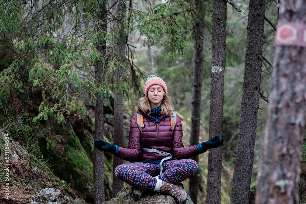 woman solo hiking whilst meditating on a rock in a forest woman solo hiking whilst meditating on a rock in a forest