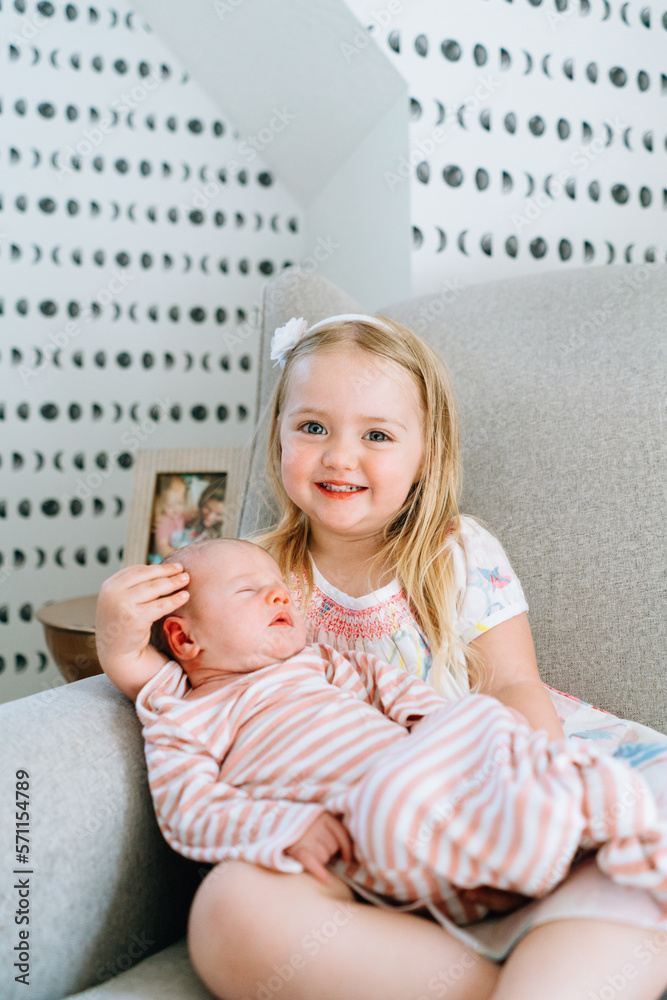 © Cavan Images - A young girl smiling at the camera while holding her baby sister
