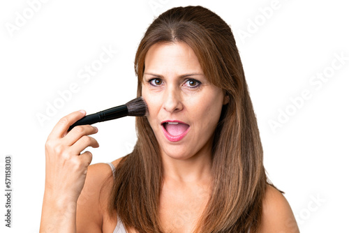 Middle age woman over isolated background holding makeup brush and surprised