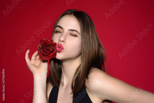 Love, air kiss. Beauty studio portrait. Beautiful model with red rose flower, isolated on red studio background. Charming young girl with perfect makeup. © Volodymyr