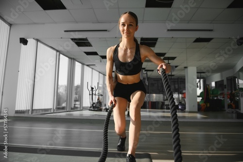 Athletic Female in a Gym Exercises with Battle Ropes During Her Fitness Workout High-Intensity Interval Training. She's Muscular and Sweaty