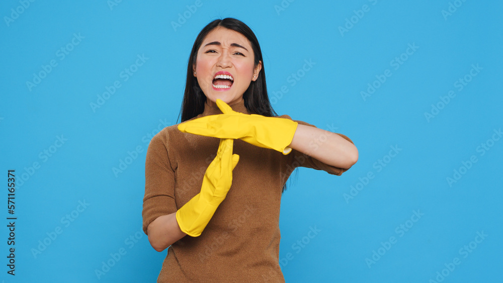 Asian homemaker doing time out gesture during house cleaning in studio over blue background. Tired housewife needed pause from work, used only the best cleaning products and equipment