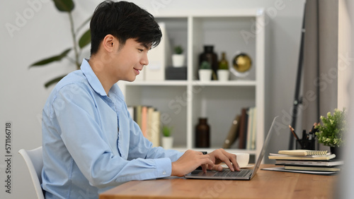 Pleasant young business man communicating in social network, searching information online on laptop computer