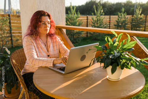 Work from home or study online with a woman gardener working at laptop outdoor on terrace, sitting on ratang chair around houseplant and flower pots photo