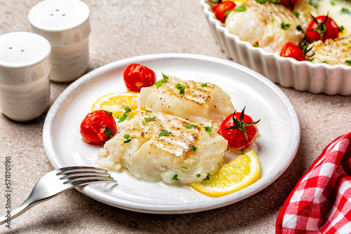 Plate with baked fillet of cod fish, with lemon, tomatoes, olive oil, salt and pepper. Mediterranean food.