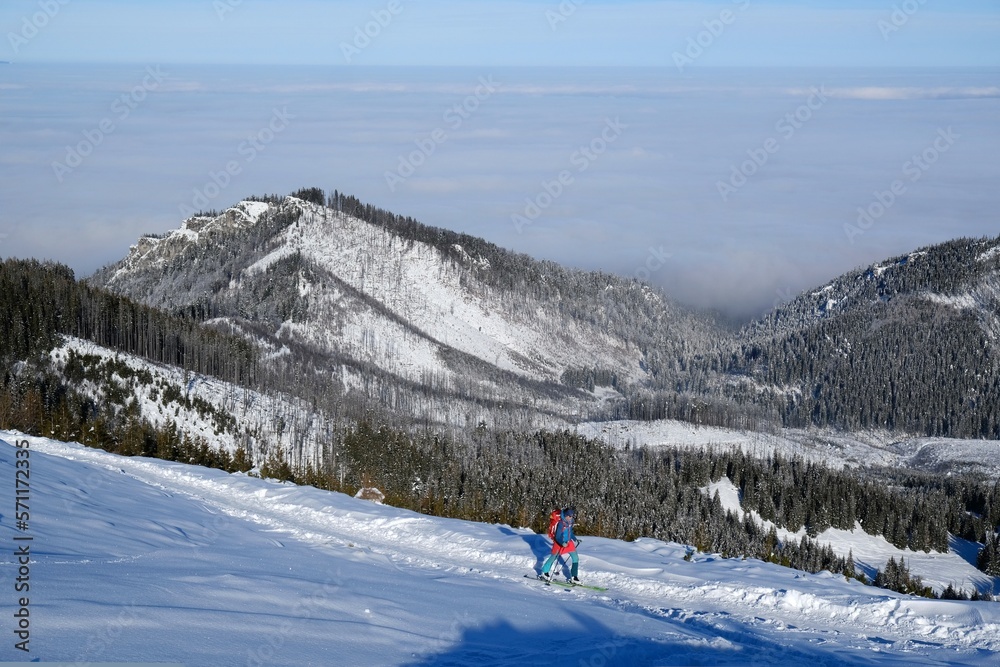 Panorama from trail to Hala Gasienicowa in Tatra Mountains in winter scenery. Babia Gora Peak on horizon. Tatra National Park, Poland. Interesting phenomenon of inversion with clouds. People on trail.