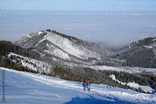 Panorama from trail to Hala Gasienicowa in Tatra Mountains in winter scenery. Babia Gora Peak on horizon. Tatra National Park, Poland. Interesting phenomenon of inversion with clouds. People on trail.