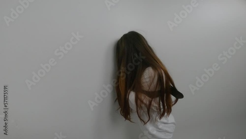 Young woman with face covered with  long red hair, dressed in straitjacket,  tied with straps, standing in  Ward in mental hospital banging her head against the wall , hands of doctor calming her