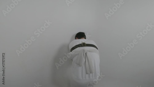 Rear view of unrecognizable psychiatric patient. Young caucasian man banging his head against wall  in white ward of asulym. Treatment of schizophrenia in psychiatric clinic
