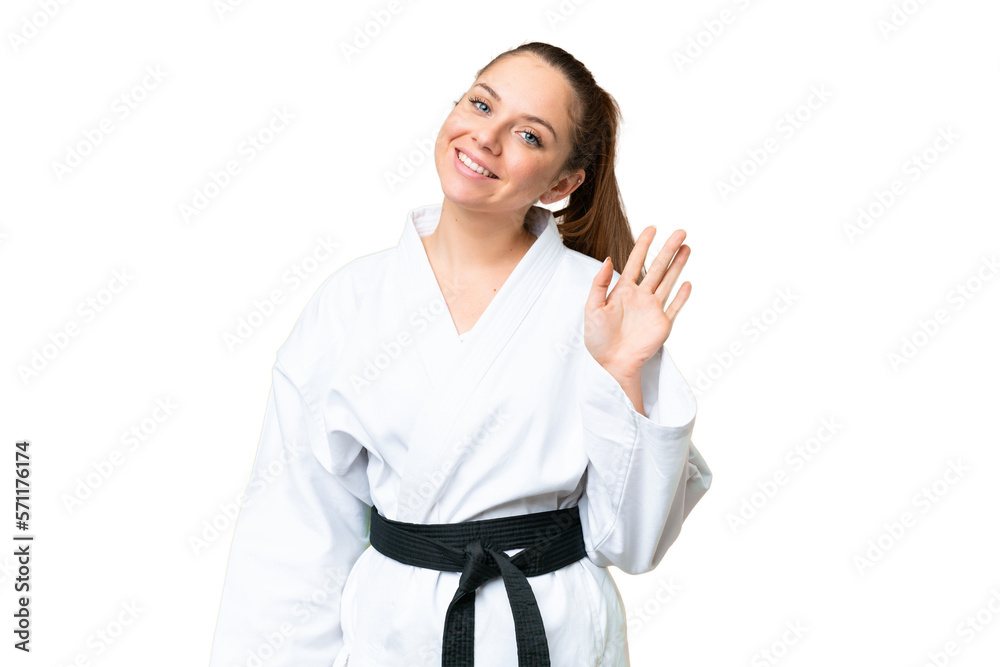 Young blonde woman doing karate over isolated chroma key background saluting with hand with happy expression