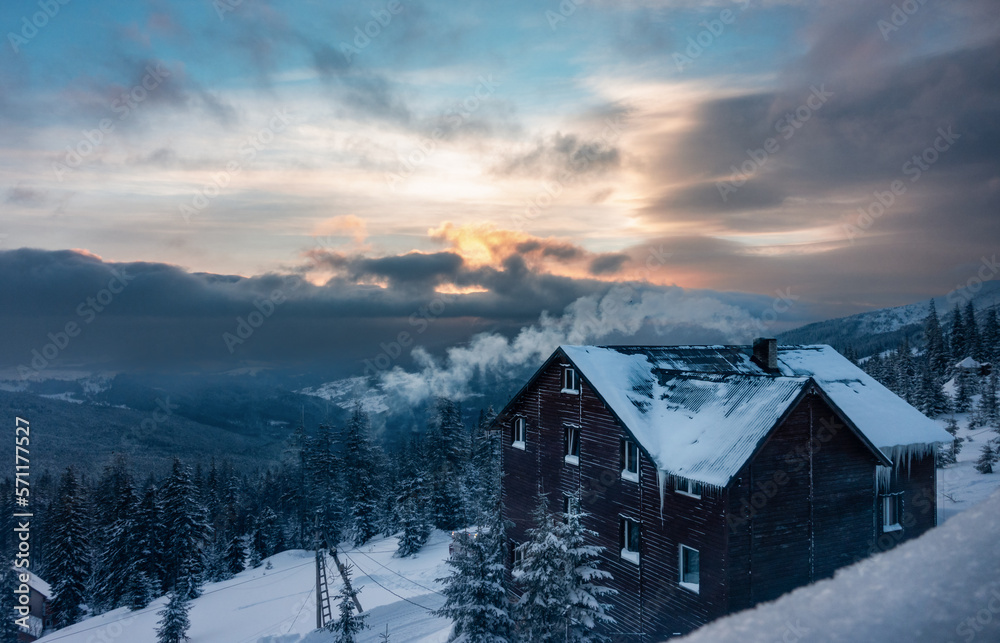 Mountains Sunrise with Log Cabin on Foreground. Fast Clouds Moving Over The Rising Sun. Scenic View in Carpathians