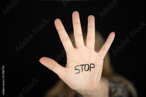 Woman showing hand stop sign with word STOP written to campaign against gender violence and pain. Hand raised to dissuade for self harm awareness, stop abusing, bullying, mental health. Copy space.