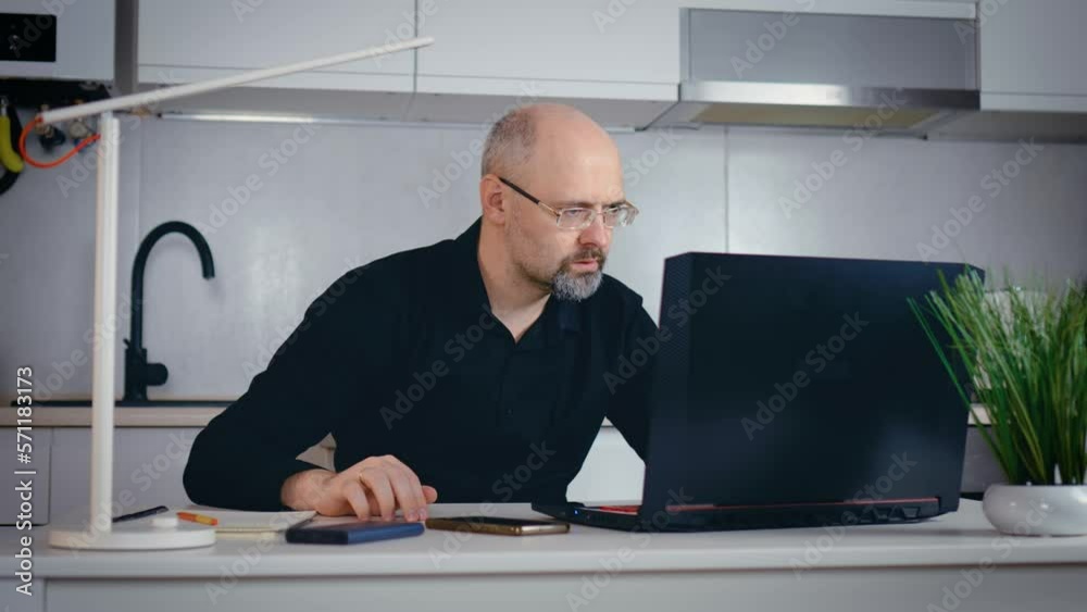 Smiling man typing on laptop in home office writing notes serious businessman working with notebook indoor. Busy worker freelancer entrepreneur working home at kitchen in financial sphere Smiling man typing on laptop in home office writing notes serious businessman working with notebook indoor. Busy worker freelancer entrepreneur working home at kitchen in financial sphere