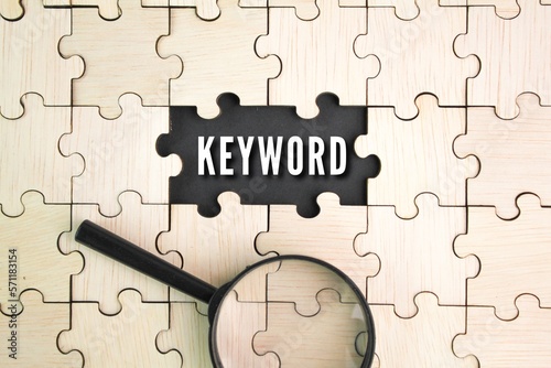 wooden puzzle and a magnifying glass with the word keyword in the middle hole of the puzzle. the concept of searching for keywords