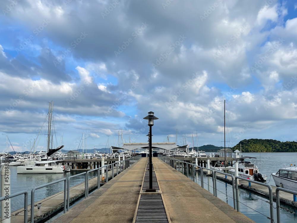 Pier and yachts. Beautiful sky with clouds. Empty modern pier with railings and beautiful lanterns stretching into the distance. Boats on both sides. Sea bay. Quiet harbor. Sailboats. View to the sea.