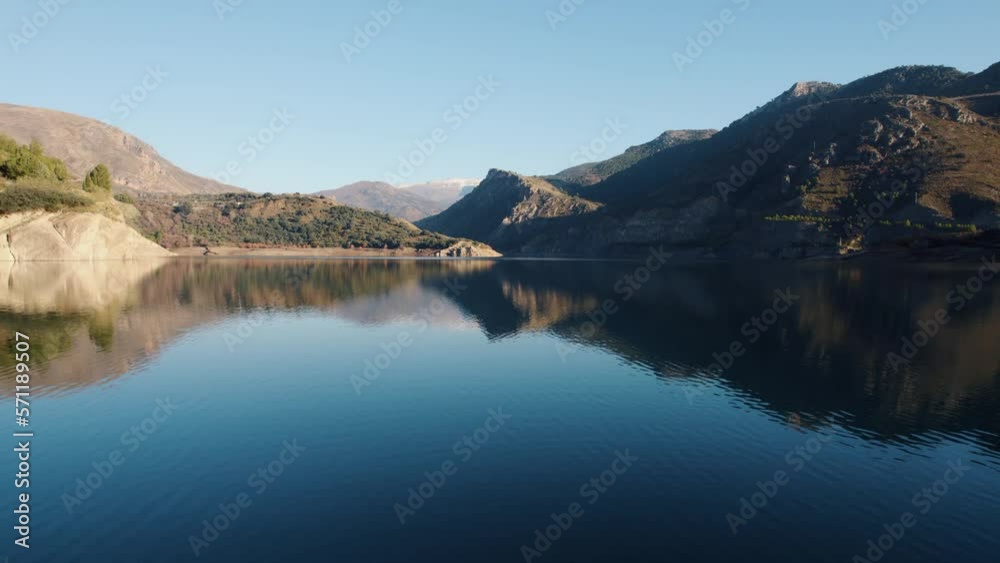 Aerial view flying across Canales reservoir calm water with reflections of Spanish Sierra Nevada mountains Aerial view flying across Canales reservoir calm water with reflections of Spanish Sierra Nevada mountains