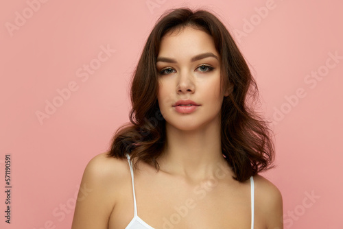 Closeup portrait of young beautiful girl with long dark hair looking at camera over pink background. Concept of beauty, skin care, cosmetology, wellness, makeup